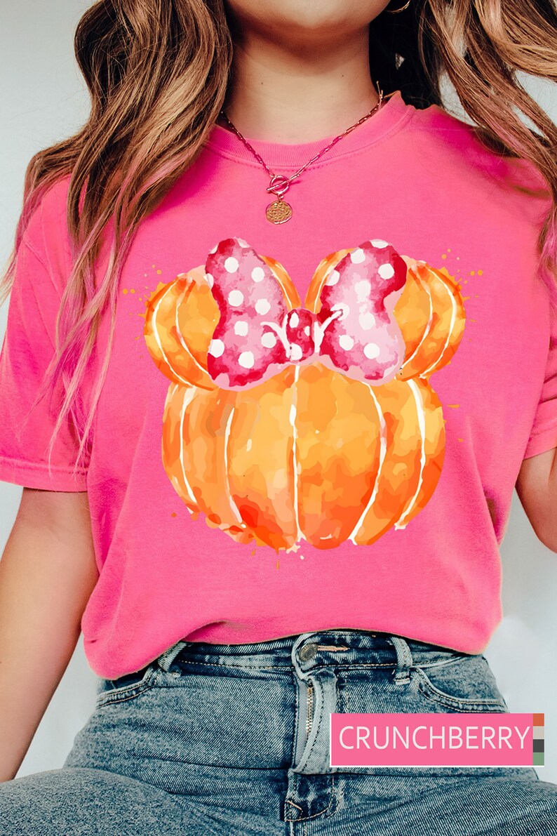 Op de afbeelding: Felroze T-shirt met een aquarelontwerp van een pompoen en een roze stippenstrik. De pompoen is oranje met een aquareleffect. Het shirt heeft een ronde hals.