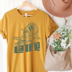 May include: A mustard yellow t-shirt with a green alligator graphic and the text "See ya later".