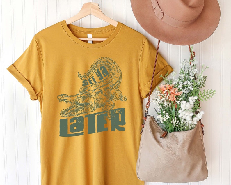 May include: A mustard yellow t-shirt with a green alligator graphic and the text "See ya later".