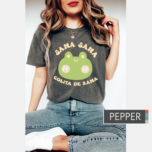 Puede incluir: Una camiseta gris oscura con un gr&aacute;fico de rana verde y el texto "Sana Sana Colita de Rana" en amarillo.