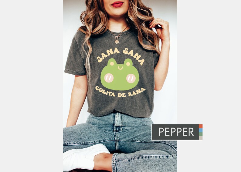Puede incluir: Una camiseta gris oscura con un gr&aacute;fico de rana verde y el texto "Sana Sana Colita de Rana" en amarillo.