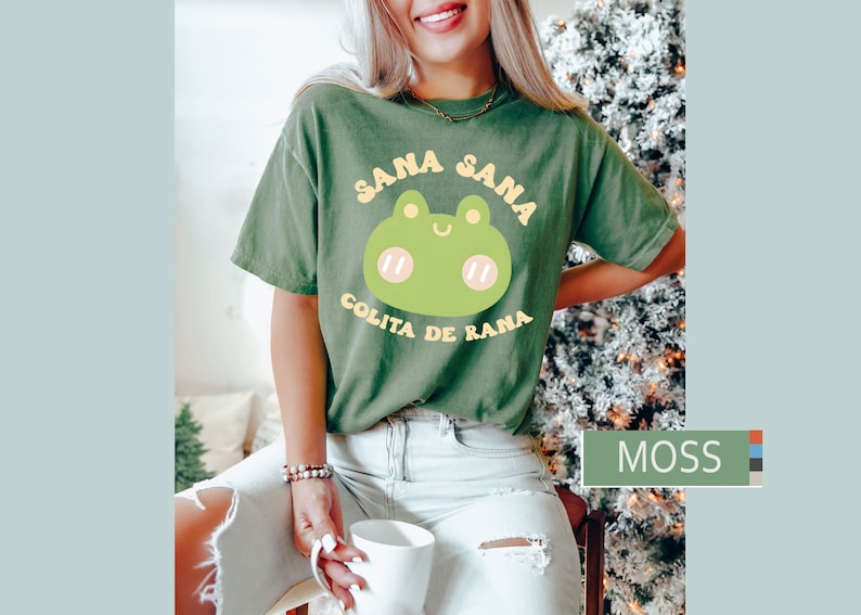 Puede incluir: Una camiseta verde con una rana de dibujos animados y el texto "Sana Sana Colita de Rana" en letras amarillas y blancas.