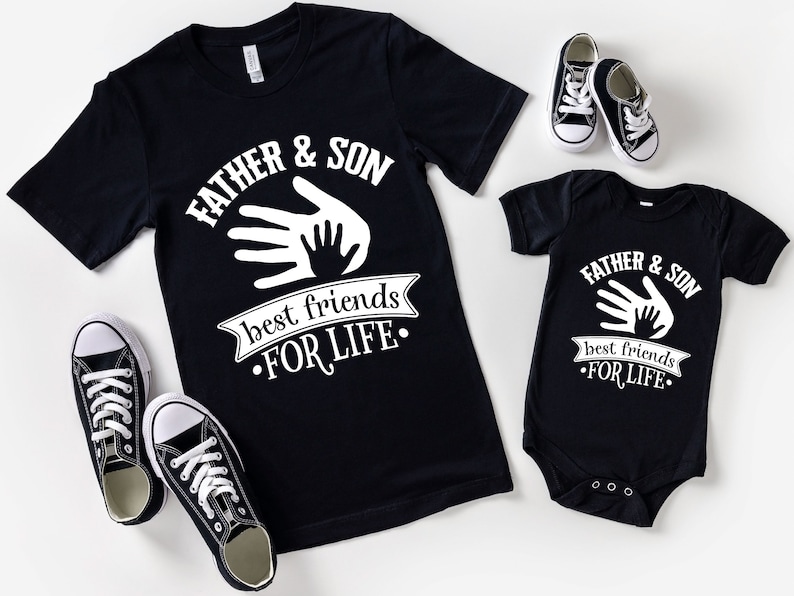 May include: Black matching t-shirts and a onesie with the text "FATHER & SON best friends FOR LIFE" in white. The design includes handprints. A pair of black sneakers and baby shoes are also in the image.