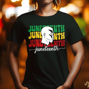 May include: A black t-shirt with a graphic design featuring the word "Juneteenth" repeated three times in red, yellow, and green, with a silhouette of a Black person's head in white. The word "Juneteenth" is also written in cursive below the graphic.