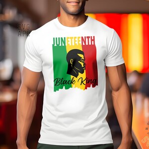 May include: A white t-shirt with a graphic design featuring a black silhouette of a man's head with the text "Juneteenth Black King" in black lettering. The graphic is set against a background of red, yellow, and green stripes.