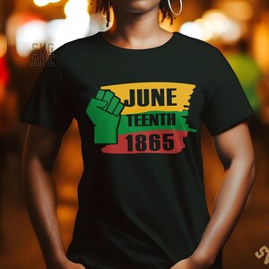Può includere: Una maglietta nera con una grafica verde, gialla e rossa che dice "Juneteenth 1865". La grafica include anche un pugno alzato.