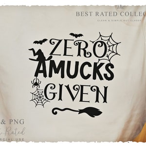 May include: Cream-colored t-shirt with the phrase "ZERO AMUCKS GIVEN" in black, featuring Halloween-themed graphics like bats, a witch, spiderwebs, a spider, and a broom. The shirt also has the text "The BEST RATED COLLECTION" and "CLEAN & SIMPLE BUT CLASSY".