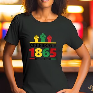 Può includere: Maglietta nera con un design grafico rosso, giallo e verde. Il grafico presenta tre pugni alzati e il testo "Celebrate 1865 - Juneteenth".