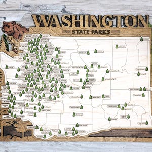 May include: A wooden map of Washington State Parks with the names of each park printed on the map. The map is surrounded by a brown frame and features a bear in the upper left corner.