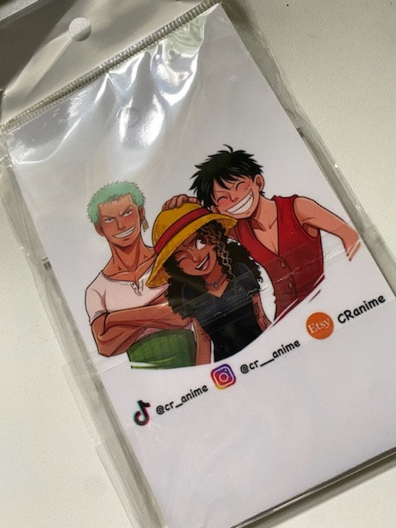May include: A white card with a colorful illustration of three anime characters. The characters are smiling and standing together. The card has social media handles for @cr_anime on TikTok, Instagram, and Etsy.