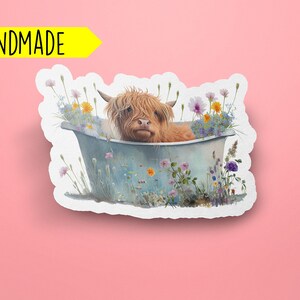 May include: A handmade sticker featuring a Highland cow taking a bath in a blue tub surrounded by colorful wildflowers.