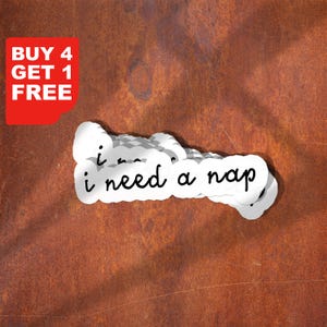 May include: A set of five white stickers with the text "i need a nap" written in black cursive. The stickers are arranged in a staggered pattern on a rusty metal surface.