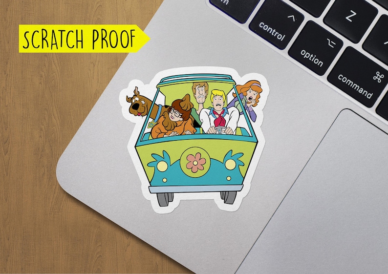 May include: A sticker featuring the Mystery Machine from Scooby-Doo. The van is green and blue with a flower on the front. The characters Scooby-Doo, Shaggy, Fred, Daphne, and Velma are inside the van.