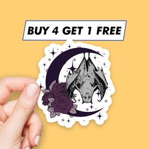 May include: A sticker featuring a black bat hanging upside down from a crescent moon with purple roses and white stars on a white background.