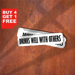以下が含まれることがあります： 「DRINKS WELL WITH OTHERS」のテキストが黒で書かれた白いステッカー。赤いコーナーグラフィックには「BUY 4 GET 1 FREE」と書かれています。ステッカーは、質感のある錆びた茶色の背景に重ねられています。