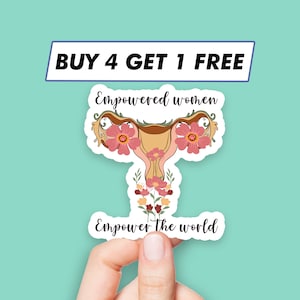 Puede incluir: Una pegatina con una ilustración estilizada de un útero con acentos florales en rosa y marrón. Se incluye el texto "Empowered women" y "Empower the world". Una pancarta en la parte superior dice "BUY 4 GET 1 FREE".