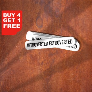 Op de afbeelding: Witte stickers met de woorden "Introvert Extrovert" liggen op een roestbruin oppervlak. Een rode hoekafbeelding leest "Koop 4 krijg 1 gratis" in witte tekst. De stickers lijken gerelateerd aan persoonlijkheidskenmerken.