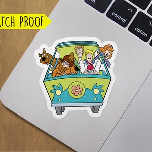 May include: A sticker featuring the Mystery Machine from Scooby-Doo. The van is green and blue with a flower on the front. The characters Scooby-Doo, Shaggy, Fred, Daphne, and Velma are inside the van.