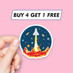 May include: A white space shuttle with a red and yellow flame trail, launching into a dark blue space with stars and planets. The sticker says "BUY 4 GET 1 FREE".