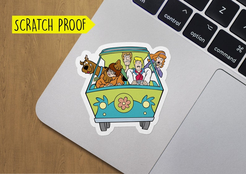 May include: A sticker featuring the Mystery Machine from Scooby-Doo. The van is green and blue with a flower on the front. The characters Scooby-Doo, Shaggy, Fred, Daphne, and Velma are inside the van.