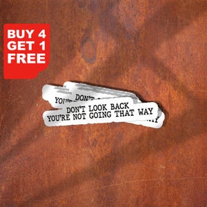 Puede incluir: Un fondo marrón oxidado con pegatinas blancas que dicen "DON'T LOOK BACK YOU'RE NOT GOING THAT WAY." Un gráfico rojo en la esquina dice "BUY 4 GET 1 FREE."