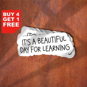 Peut inclure: Plusieurs autocollants blancs en forme de nuage avec le texte "IT'S A BEAUTIFUL DAY FOR LEARNING" sont superposés sur un fond brun texturé. Un coin rouge indique "BUY 4 GET 1 FREE". Ces autocollants sont à usage éducatif.