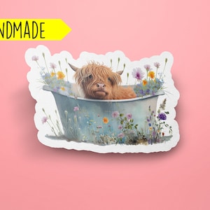K&ouml;nnte beinhalten: Ein handgemachtes Sticker mit einer schottischen Hochlandkuh, die in einer blauen Wanne badet, umgeben von bunten Wildblumen.