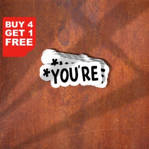 Może przedstawiać: Białe naklejki z czarnym tekstem "*YOU'RE;" z gwiazdkami. Czerwony prostokąt z białym tekstem "BUY 4 GET 1 FREE" znajduje się w lewym górnym rogu. Tło jest w kolorze rdzawego brązu.