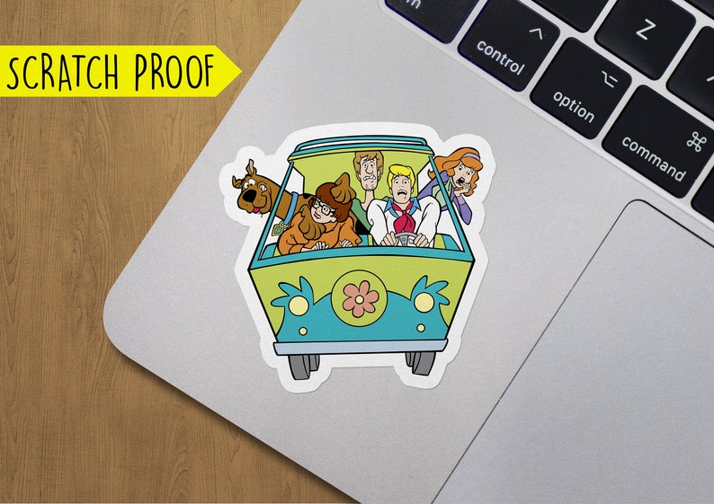 May include: A sticker featuring the Mystery Machine from Scooby-Doo. The van is green and blue with a yellow flower on the front. The characters Scooby-Doo, Shaggy, Fred, Daphne, and Velma are inside the van.