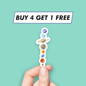 Puede incluir: Una mano sostiene una pegatina de los planetas de nuestro sistema solar, con el texto "BUY 4 GET 1 FREE" encima.