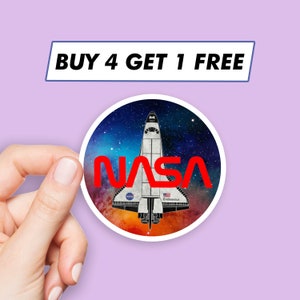 May include: A round sticker with a white space shuttle against a dark blue and purple galaxy background. The word "NASA" is in red letters across the shuttle. The sticker has a white border.