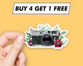 May include: A sticker featuring a vintage camera with watercolour flowers in shades of pink, purple, and green. The text "BUY 4 GET 1 FREE" is printed on a blue banner above the camera.