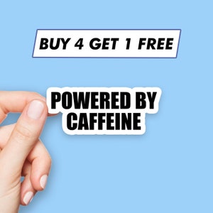 Puede incluir: Pegatina blanca con texto negro que dice "Powered by Caffeine". Una mano sostiene la pegatina. Encima de la pegatina hay un rectángulo blanco con texto azul que dice "Buy 4 Get 1 Free".