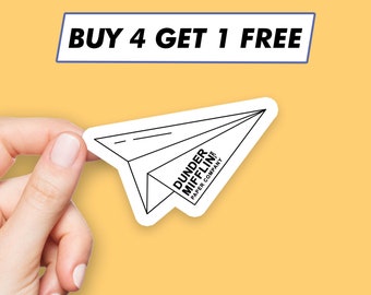 May include: A white paper airplane sticker with black outline and text that reads "Dunder Mifflin Paper Company" and "Buy 4 Get 1 Free" in a blue rectangle.