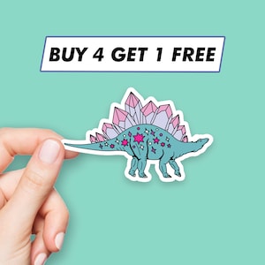May include: A sticker featuring a blue dinosaur with pink crystals on its back and pink stars on its body. The sticker has a white outline and the text "BUY 4 GET 1 FREE" is printed on a blue rectangle above the dinosaur.