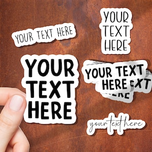 Peut inclure: Plusieurs autocollants blancs avec le texte noir "YOUR TEXT HERE". Les autocollants sont de différentes formes et tailles, avec une police manuscrite et une police en gras. Sur un fond marron.