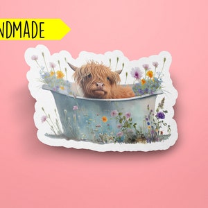 May include: A handmade sticker featuring a Highland cow taking a bath in a blue tub surrounded by colorful wildflowers.