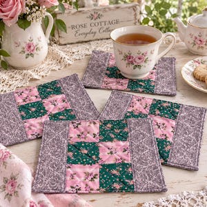 May include: A set of three rectangular fabric coasters featuring a quilted patchwork design. The coasters are constructed with alternating squares of dark green floral fabric and light pink floral fabric, bordered by a grey damask patterned fabric.