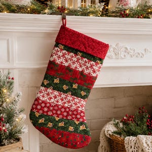 May include: A quilted Christmas stocking featuring horizontal stripes of red, white, and dark green fabric with patterns of snowflakes, holly leaves, and berries. The stocking has a solid red cuff at the top and a small red fabric hanging loop.