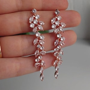 May include: Rose gold dangle earrings with a cascading design of clear cubic zirconia stones.