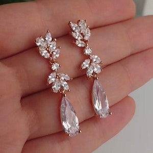 May include: Rose gold dangle earrings with clear cubic zirconia stones in a floral design. The earrings have a teardrop-shaped stone at the bottom.