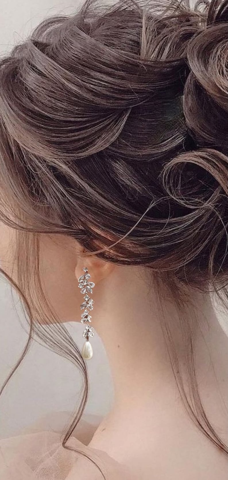May include: A pair of elegant drop earrings with a floral design, clear crystals, and a pearl drop. The earrings are set against dark brown hair. A stylish accessory for formal events, adding a touch of glamour to any outfit.