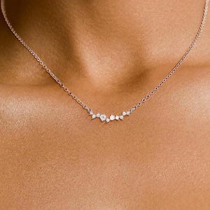 May include: A delicate silver necklace with a cluster of small, sparkling diamonds arranged in a curved line.