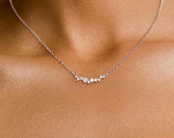 May include: A delicate silver necklace with a cluster of small, sparkling diamonds arranged in a curved line.