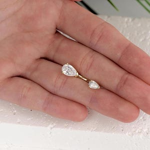 Puede incluir: Un piercing de cuerpo de oro con dos piedras preciosas transparentes en forma de pera.