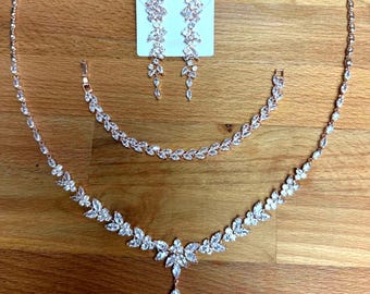 May include: A rose gold jewelry set consisting of a necklace, a bracelet, and a pair of drop earrings. Each piece features a leaf-like design set with clear, marquise-cut crystals. The necklace includes a central pear-shaped crystal drop.
