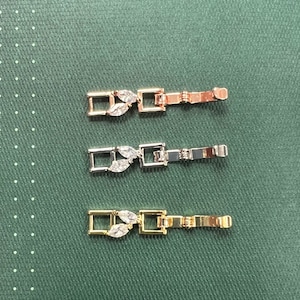 May include: Three watch band clasps with a leaf design and clear rhinestones. The clasps are in rose gold, silver, and gold.