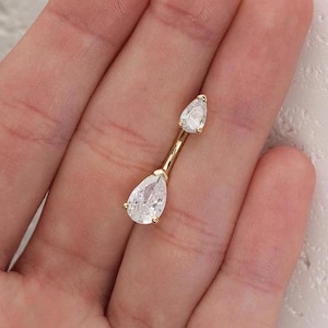 Puede incluir: Un anillo de ombligo de oro con dos piedras transparentes en forma de l&aacute;grima.