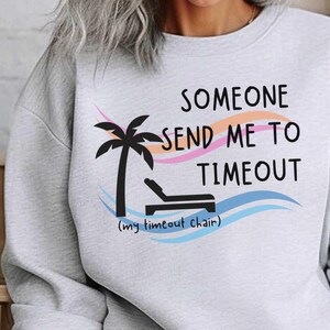 May include: Gray sweatshirt with the text "Someone send me to timeout (my timeout chair)" and a palm tree with a lounge chair underneath.