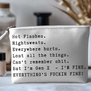 May include: A white zippered cosmetic bag with black text that reads: "Hot Flashes. Nightsweats. Everywhere hurts. Lost all the things. Can't remember shit. But I'm Gen X - I'M FINE. EVERYTHING'S FUCKIN FINE!"
